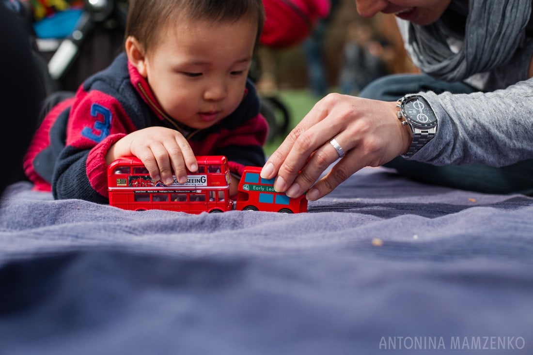 father and son playing with red london buses on a picnic rug